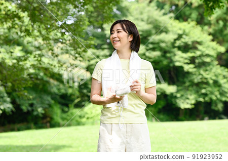 A woman using a fan in the shade of a tree 91923952