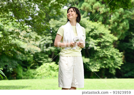 A woman using a fan in the shade of a tree A woman using a fan in the shade of a tree 91923959