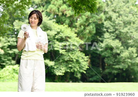A woman using a fan in the shade of a tree A woman using a fan in the shade of a tree 91923960