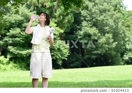 Woman hydrating in the shade of a tree Woman hydrating in the shade of a tree 91924413