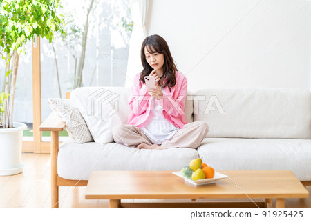 A young woman operating a smartphone in a room 91925425