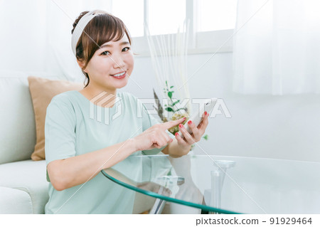 A smiling Japanese woman using a smartphone at home (app) 91929464