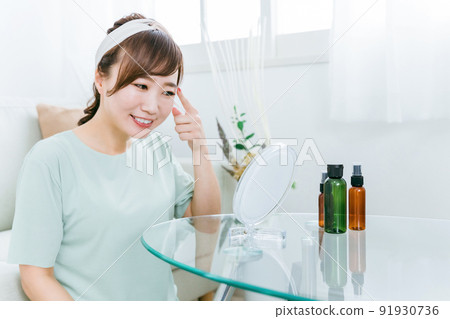 A woman looking in the mirror with a smile at home (eyes / contact lenses) 91930736