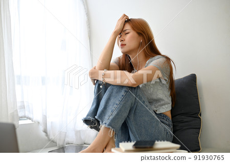 Frustrated young Asian woman sitting in her home living room, thinking her life problems 91930765