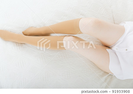 Knee socks or socks. Beige compression stockings on a woman in a white room. Girl putting on stockings at home. Beautiful female legs. Knee socks or socks. Beige compression stockings on a woman in a white room. Girl putting on stockings at home. Beautiful female legs. 91933908