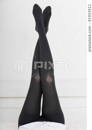 Beautiful woman putting on stocking indoors, closeup. Beautiful long female legs in stockings. Girl putting on stockings at home in a white room. Black tights. Beautiful woman putting on stocking indoors, closeup. Beautiful long female legs in stockings. Girl putting on stockings at home in a white room. Black tights. 91933911