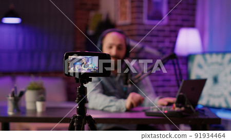 Selective focus on digital video camera screen recording influencer caucasian man streaming live talk show using microphone from home studio. Male content creator filming vlog for social media post. 91934464