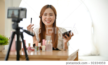 Charming Asian female beauty blogger applying cosmetics, recording makeup video. Charming Asian female beauty blogger applying cosmetics, recording makeup video. 91934959