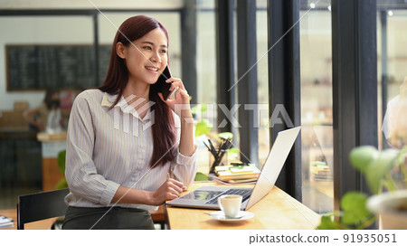 Successful young asian woman investor having phone conversation and using laptop at coffee shop 91935051