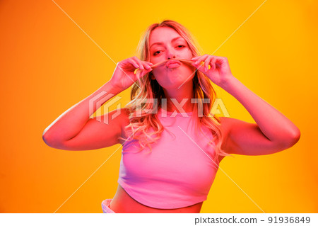 Portrait of young beautiful woman posing isolated over yellow background in neon light. Making funny faces Portrait of young beautiful woman posing isolated over yellow background in neon light. Making funny faces 91936849
