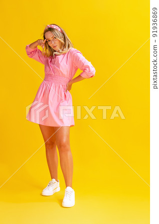 Portrait of beautiful young woman in cute pink dress posing isolated over yellow studio background Portrait of beautiful young woman in cute pink dress posing isolated over yellow studio background 91936869
