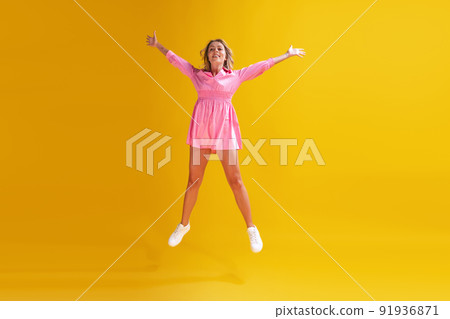 Portrait of beautiful young woman in cute pink dress posing isolated over yellow studio background. Delightful 91936871