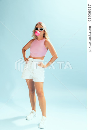 Portrait of stylish young woman in trendy sunglasses posing with bubble gum isolated over light blue studio background 91936917