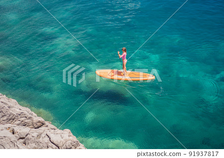 Young women Having Fun Stand Up Paddling in blue water sea in Montenegro. SUP. girl Training on Paddle Board near the rocks 91937817