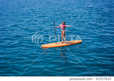 Young women Having Fun Stand Up Paddling in blue water sea in Montenegro. SUP. girl Training on Paddle Board near the rocks 91937820
