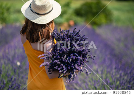 Girl in a yellow dress and a straw hat with a huge bouquet of lavender flowers. 91938845
