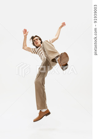 Portrait of expressive young man in vintage outfit dancing, posing isolated over white studio background. Buttom view 91939003