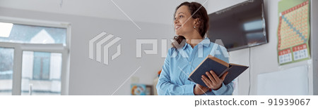 Happy afro female teacher with book in a light elementary school classroom 91939067