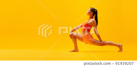Portrait of young slim, flexible girl in shorts doing stretching exercises isolated on bright yellow background. Sport, health, active lifestyle Portrait of young slim, flexible girl in shorts doing stretching exercises isolated on bright yellow background. Sport, health, active lifestyle 91939207