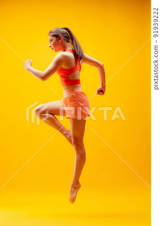 Full-length portrait of young sportive girl in motion isolated on bright yellow background. Modern sport, action, motion, summer, vacation, youth concept. 91939222