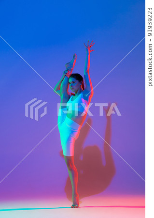 Studio shot of young flexible girl in fitness sport uniform practicing isolated on gradient pink-purple background in neon light. Sport, beauty, ad 91939223