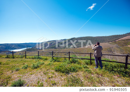 The resting place with a beautiful view of the mountain near the Zezere river. A man tourist takes a photo. Ferreira do Zezere, Portugal 91940305