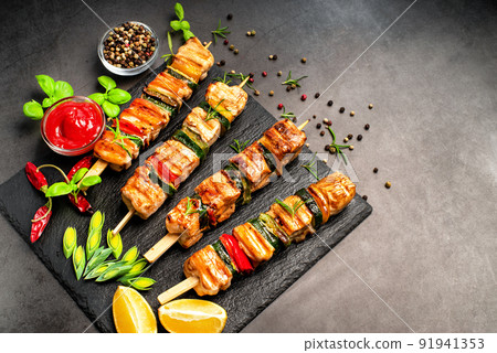Grilled kebab pieces with vegetables on skewers on a ceramic black board on a dark background with fresh basil leaves.Grilled pieces of chicken meat on skewers. 91941353