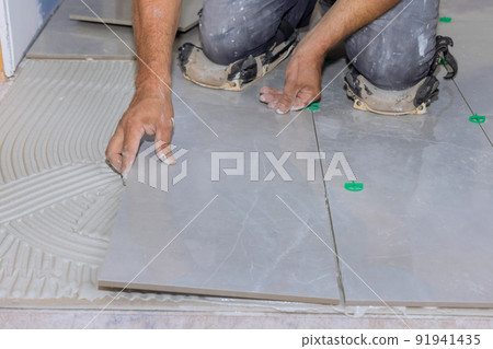 Installing ceramic tiles on an adhesive surface while working on the construction 91941435