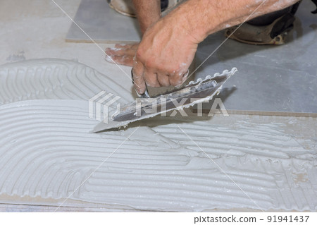 Putting adhesive on the bathroom floor by spreading wet mortar before applying tiles Putting adhesive on the bathroom floor by spreading wet mortar before applying tiles 91941437
