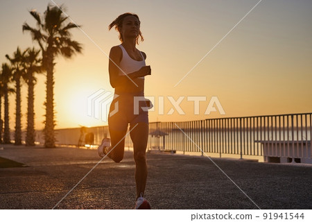 Silhouette of young woman jogging on shore at sunrise. 91941544
