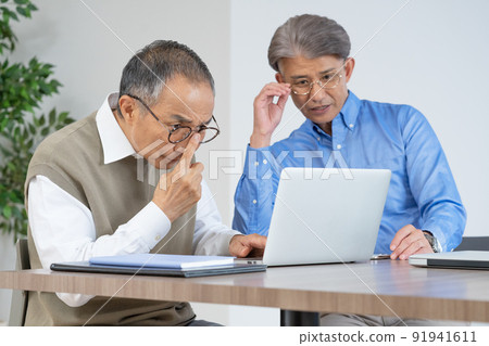 Two senior men with presbyopia looking at a computer wearing glasses in the living room at home 91941611