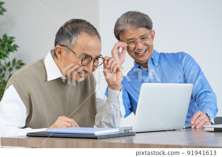 Two senior men with presbyopia looking at a computer wearing glasses in the living room at home 91941613