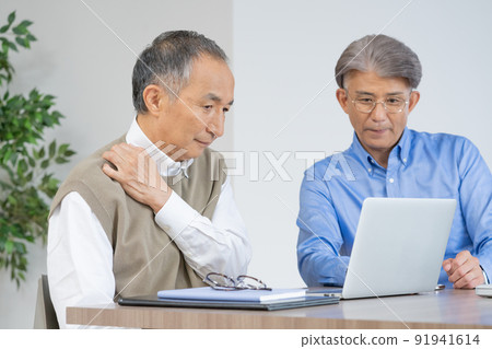 Senior men with presbyopia and stiff shoulders looking at a computer in the living room at home Senior men with presbyopia and stiff shoulders looking at a computer in the living room at home 91941614