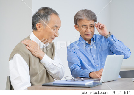 Senior men with presbyopia and stiff shoulders looking at a computer in the living room at home 91941615