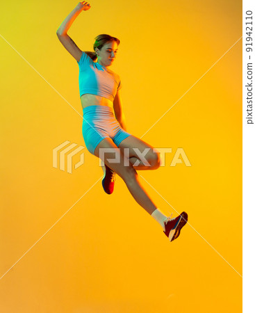 Professional longjumper. One female athlete in sports uniform jumping isolated on yellow background. Concept of sport, action, motion, speed. Professional longjumper. One female athlete in sports uniform jumping isolated on yellow background. Concept of sport, action, motion, speed. 91942110