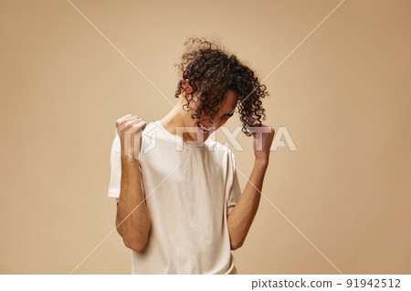 Cheerful cute awesome tanned curly man in basic t-shirt posing isolated on over beige pastel background. Fashion New Collection offer. People and Emotions concept. Free place for ad Cheerful cute awesome tanned curly man in basic t-shirt posing isolated on over beige pastel background. Fashion New Collection offer. People and Emotions concept. Free place for ad 91942512