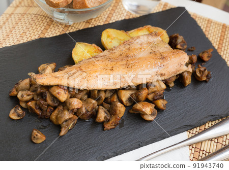 fried trout fillet on pillow of fried champignon mushrooms on dark warm stone plate 91943740