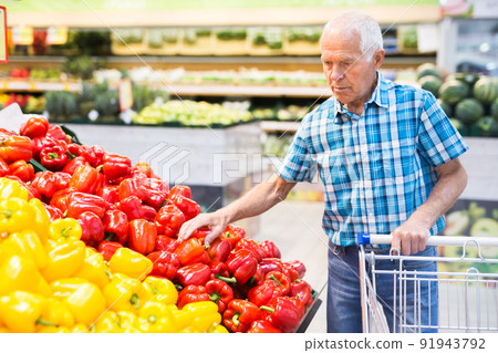 Mature senor examines bell pepper in vegetables section of supermarket 91943792