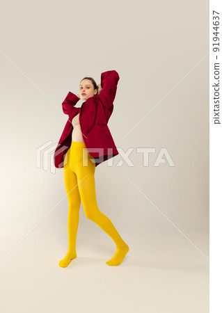 Full-length portrait of young stylish girl in yellow tights and red jacket posing isolated over grey studio background. Bright look Full-length portrait of young stylish girl in yellow tights and red jacket posing isolated over grey studio background. Bright look 91944637