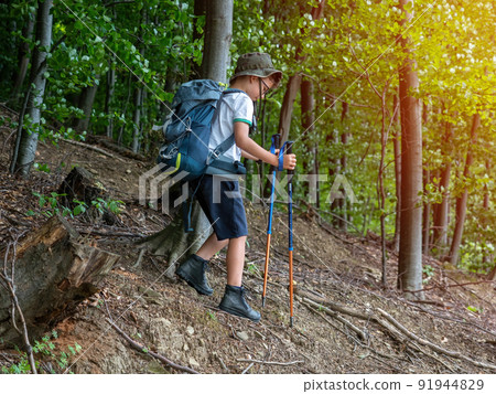 Happy boy with backpack and trekking sticks hiking in mountain forest Happy boy with backpack and trekking sticks hiking in mountain forest 91944829