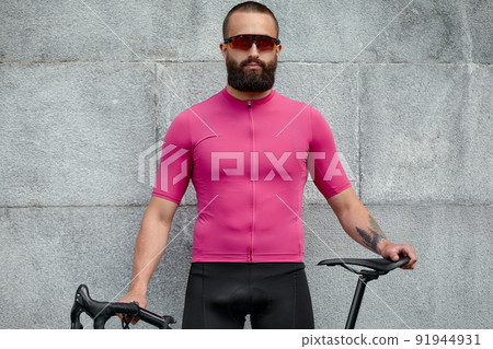 Cyclist in pink sportwear resting after an workout while standing against cement wall background with copy space area for text message or advertising 91944931