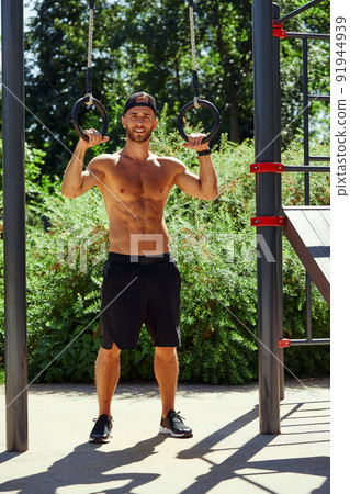 Shirtless man doing loop exercises outdoors in summer park. 91944939