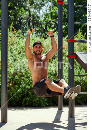 Young and handsome man is doing some push-ups. He is using loops for that Young and handsome man is doing some push-ups. He is using loops for that 91944947