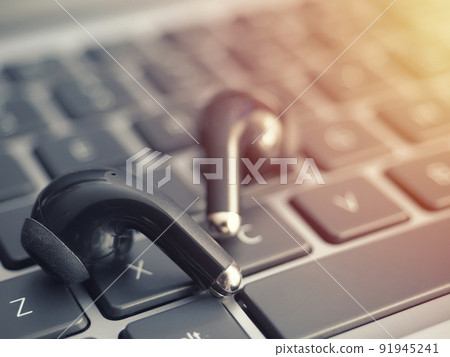 Wireless headphones on a laptop keyboard. Watching movies and listening to music on a laptop using true wireless headphones Wireless headphones on a laptop keyboard. Watching movies and listening to music on a laptop using true wireless headphones 91945241