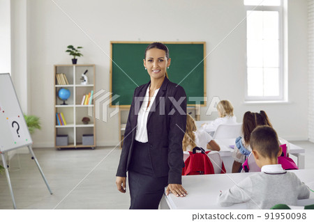 Beautiful and intelligent female primary school teacher against background of her classroom. 91950098