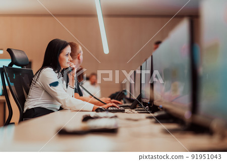 Female security guard operator talking on the phone while working at workstation with multiple displays Security guards working on multiple monitors 91951043