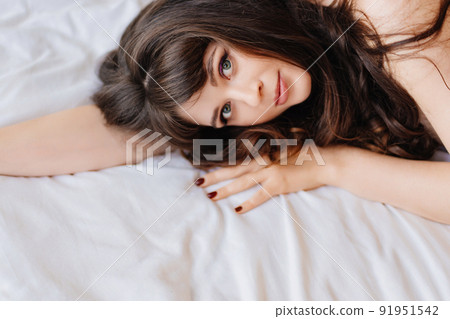 an attractive and sexy young woman with long dark hair lies in bed. bed linen. an attractive and sexy young woman with long dark hair lies in bed. bed linen. 91951542