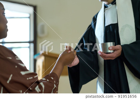 Young African American parishioner taking unleavened bread from hand of priest 91951656