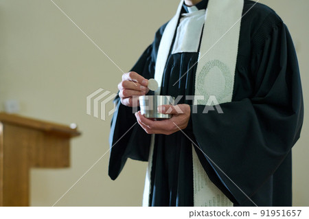 Priest of Catholic church in cassock holding small cup with unleavened bread 91951657