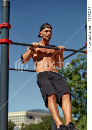 Athletic young man hanging from the bars at the calisthenics gym outdoors smiling Athletic young man hanging from the bars at the calisthenics gym outdoors smiling 91952884